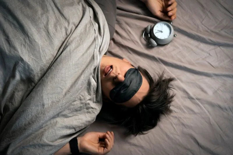 A person wearing a sleep mask, surrounded by a calming atmosphere, demonstrating how melatonin sleep support can promote restful sleep in a quiet, dark environment.