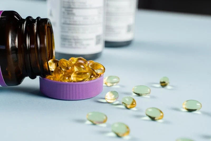 A bottle of golden-colored gel capsules spilled over with several capsules visible, representing collagen supplements for pregnancy and overall health.